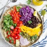 Black bean quinoa bowl with bell peppers cabbage tomatoes and black beans on white table with striped blue napkin.
