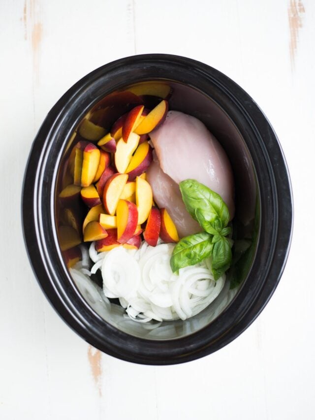 Overhead shot of a slow cooker with chicken, peaches, onion, and basil.