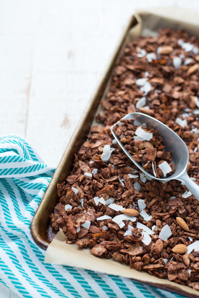 A baking sheet lined with parchment with chocolate granola topped with coconut flakes and almonds.