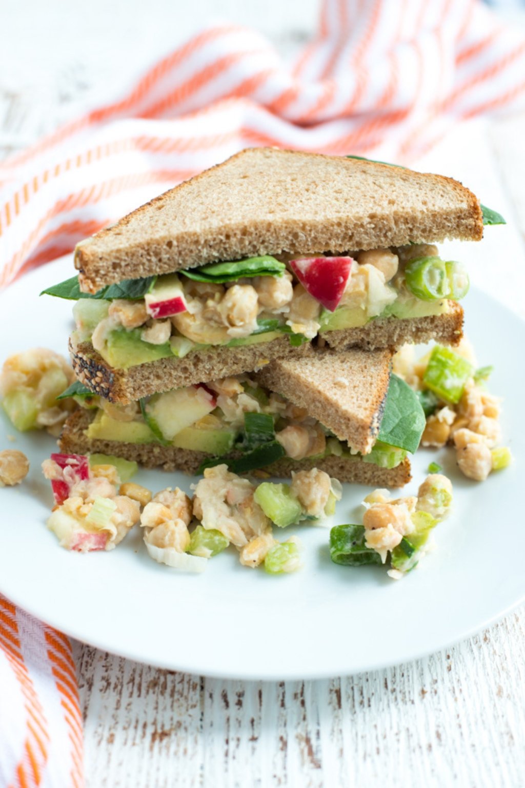 A stack of two halves of a veggie and chickpea sandwich on a plate.
