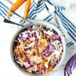Thinly sliced purple cabbage slaw with carrots in a bowl with a striped blue napkin on the side.