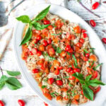 A white platter filled with shredded slow cooker balsamic chicken with tomatoes and basil, on a white background with fresh herbs.