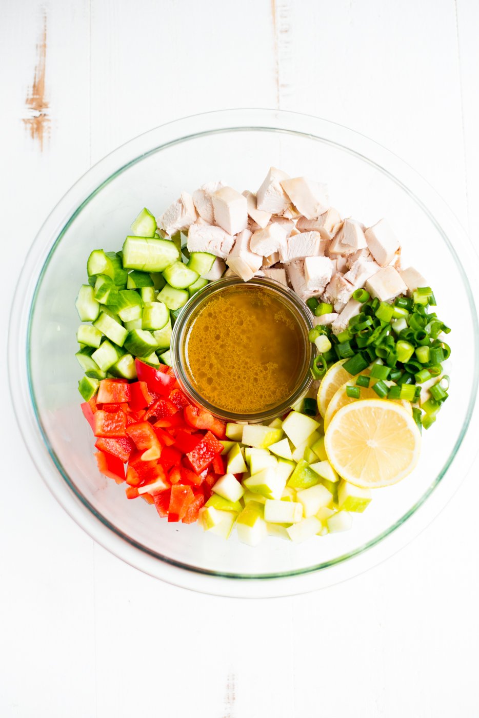 A bowl filled with chopped chicken, bell peppers, cucumbers, and sliced lemon.