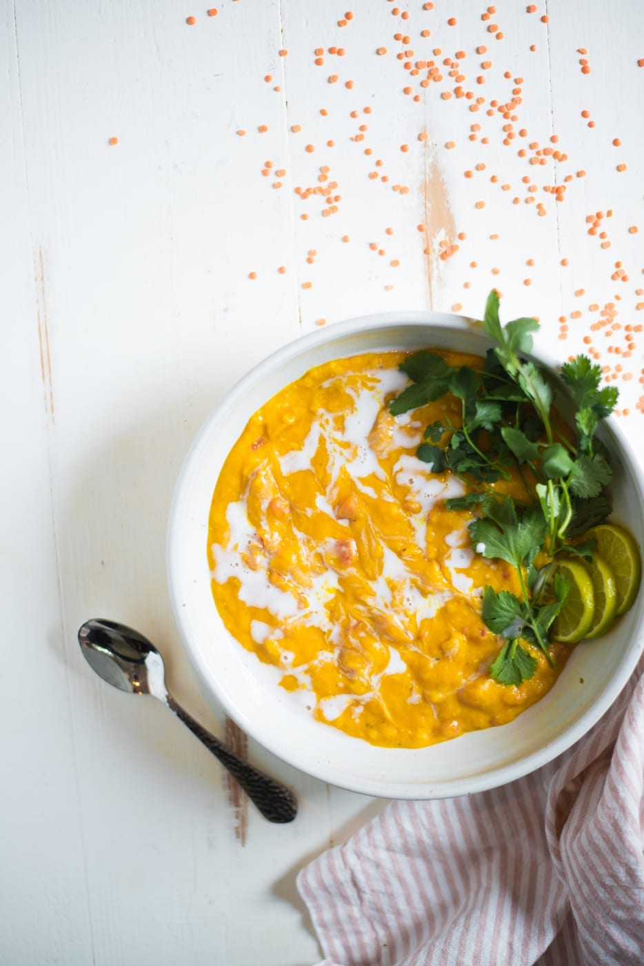 Overhead shot of red lentil soup in a white bowl garnished with cilantro and lime slices.