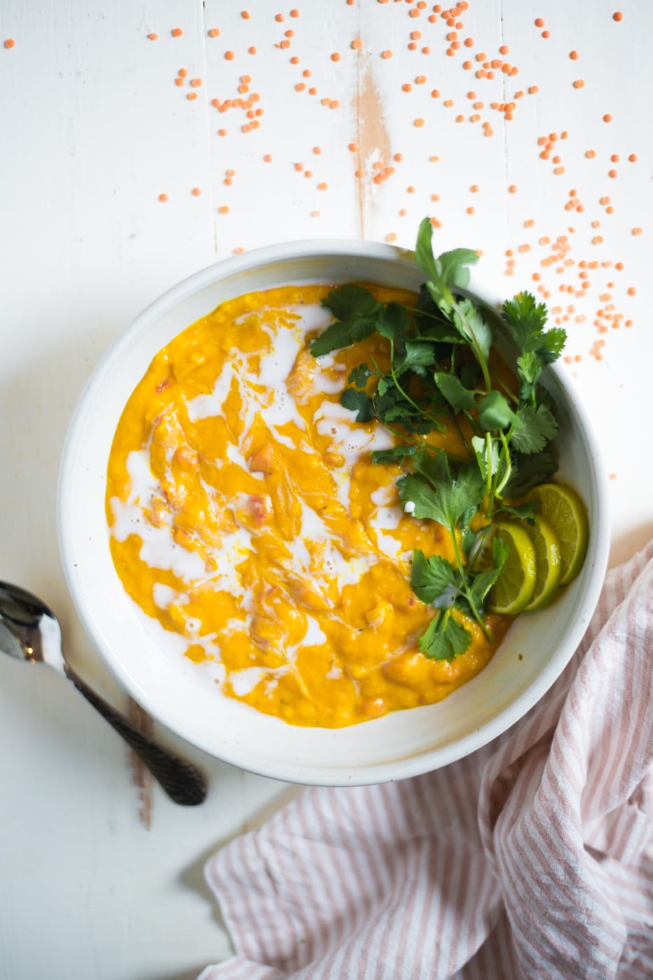 Overhead shot of red lentil soup in a white bowl garnished with cilantro and lime slices.