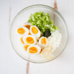 Halved hard boiled eggs in a bowl with chopped celery and onion.