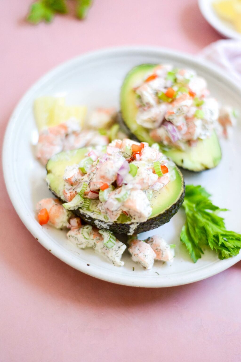 close up of two shrimp stuffed avocado halves on a white plate