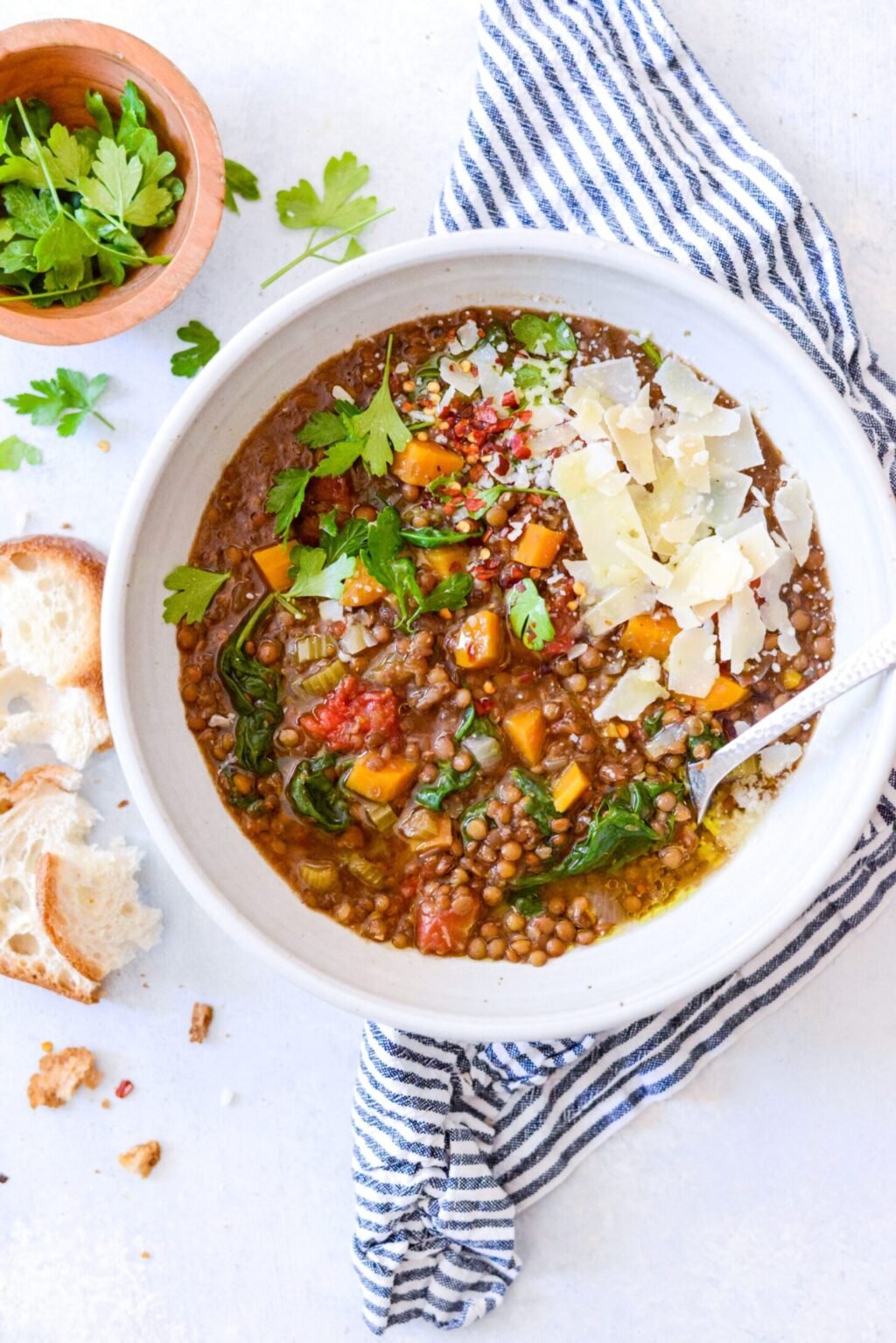 white bowl of crockpot lentil soup with fresh herbs and crusty bread on the side