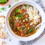 white bowl of crockpot lentil soup with fresh herbs and crusty bread on the side