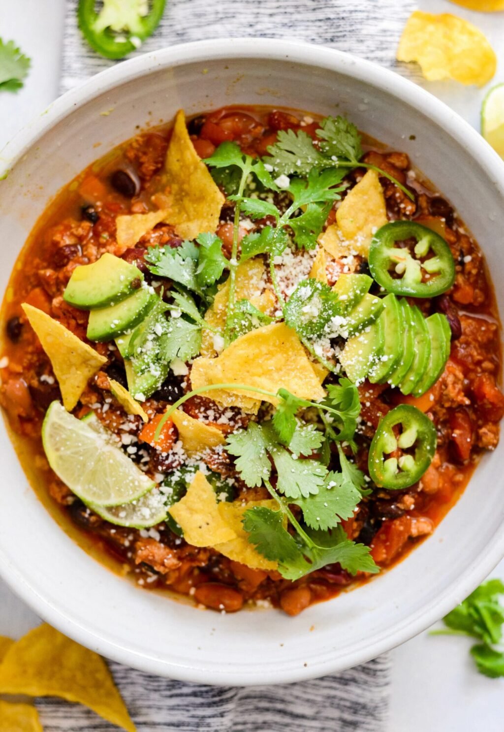 closeup view of turkey chili in a white bowl with chips and lime slices