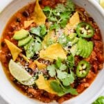closeup view of turkey chili in a white bowl with chips and lime slices
