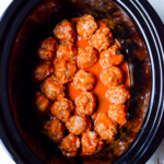 Meatballs coated in red sauce arranged in a slow cooker on a white surface.