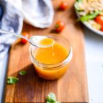 spoon dipping into a glass jar of salad dressing