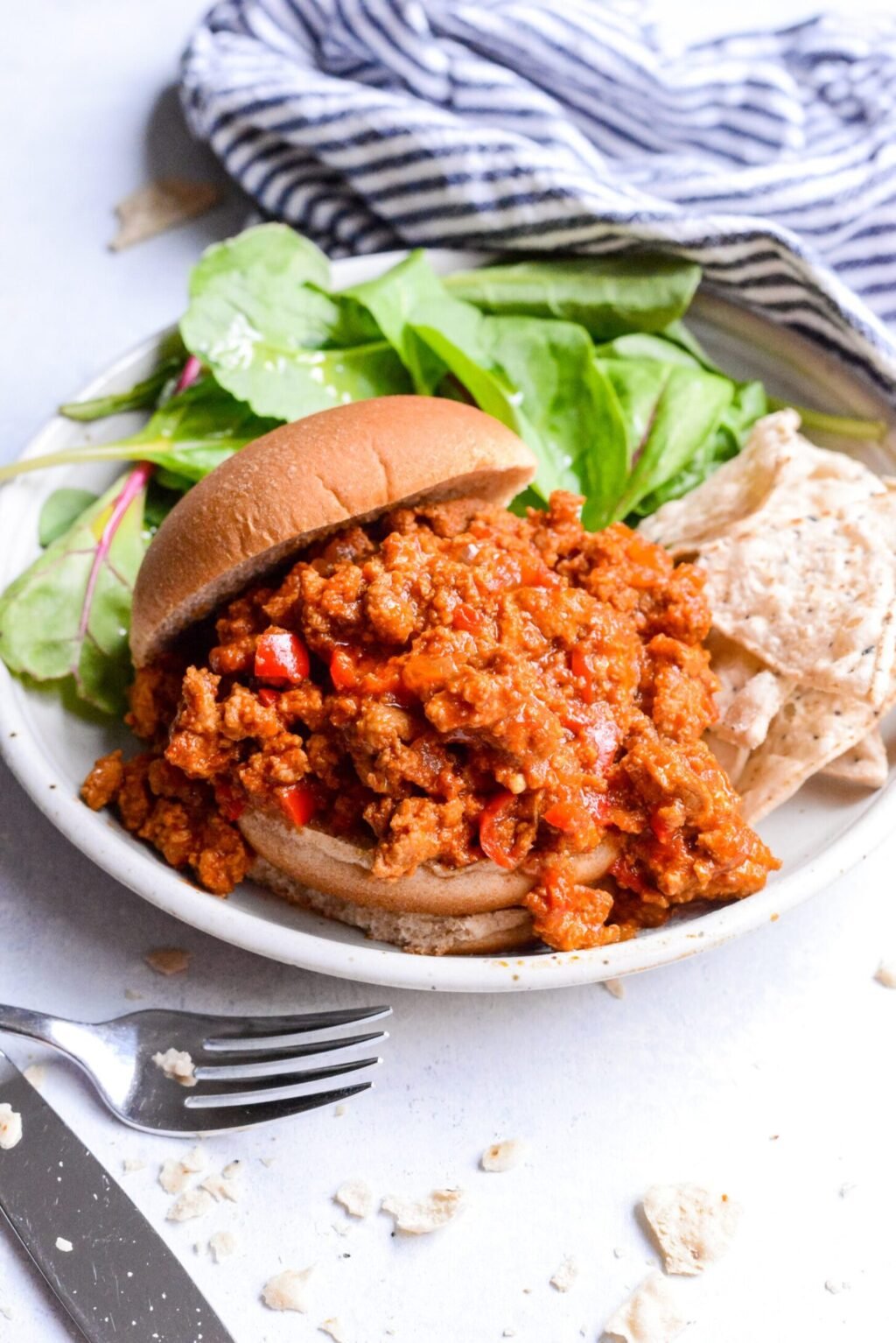 sloppy joe sandwich on a white plate with leafy greens and striped blue napkin