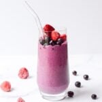 berry protein smoothie in a clear glass with a straw on white background