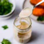 spoon full of miso tahini dressing with a glass mason jar on white background board