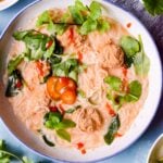 white bowl filled with soup and chicken meatballs and noodles on blue background
