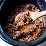 wooden spoon with ground beef and a black slow cooker