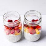 two jars with overnight oats and fruit on top with white background
