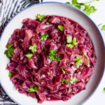 close up view of red cabbage on a white plate with fresh green herbs on top