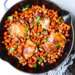 skillet chicken and sweet potatoes on a white background with fresh herbs on top and a striped blue napkin on the handle