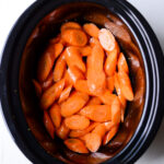 top down view of sliced carrots in a black crockpot on white background
