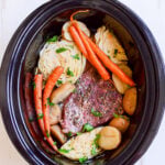 top down view of slow cooker corned beef ingredients in a black crockpot on a white background