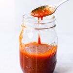 spoonful of honey sriracha sauce in a clear glass mason jar on a white background