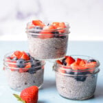 three jars of protein chia pudding topped with fresh berries on a blue and white background