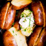 close up of slow cooker baked potatoes in a black crockpot with chives and sour cream on top