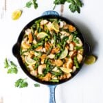 Overhead shot of a chicken and vegetable skillet dinner on a white background with fresh herbs.