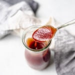 Spoonful of chipotle BBQ sauce from a glass jar, with a napkin on a white background.