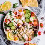 Greek Inspired Chicken Bowl in a white dish topped with yogurt tahini sauce with a blue napkin on a white background.