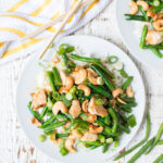 White plate with a healthy chicken cashew green bean skillet dinner, with a chopsticks and a striped napkin on the side.