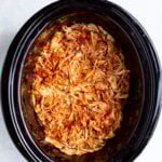 Slow cooker BBQ chicken in a black crockpot on a white background.