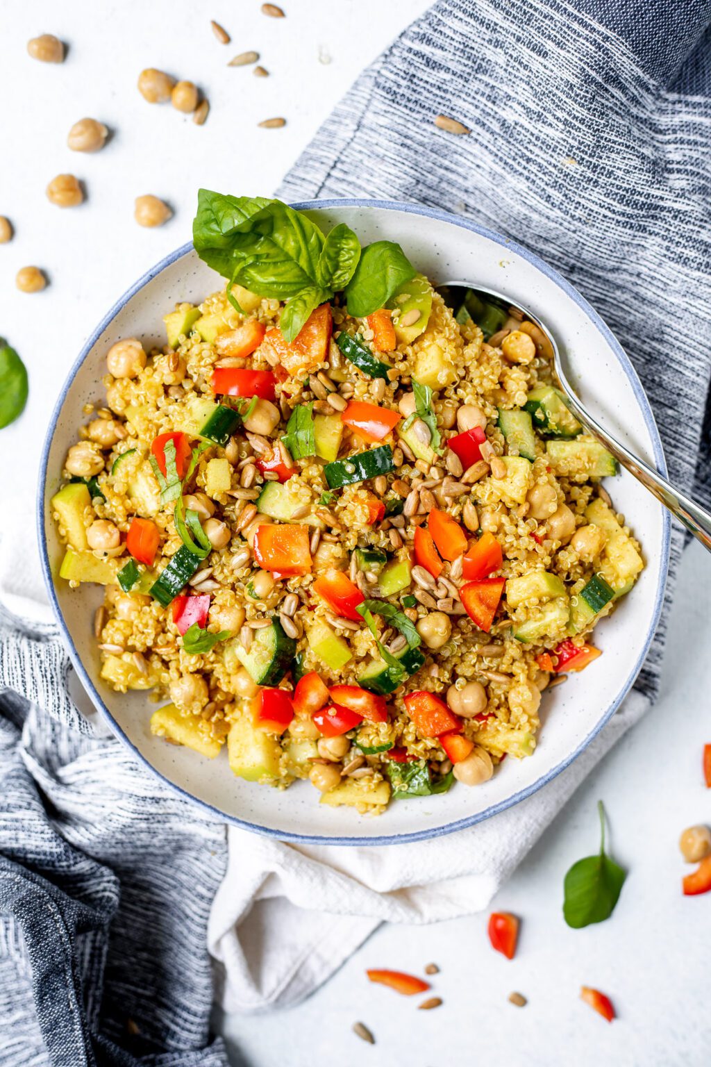 Overhead shot of blue and white bowl on a white background filled with quinoa, chopped veggies, chickpeas, and basil.