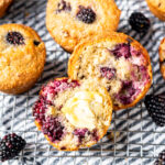 Close up of a gluten free blackberry muffin torn in half and smeared with butter, on top of a cooling rack.