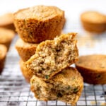 Stack of gluten free zucchini muffins sitting on top of a cooling rack, with one muffin torn in half.