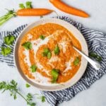Top down view of a white bowl filled with easy spiced carrot and lentil soup with fresh herbs on top.
