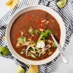 Top down view of a white bowl filled with crockpot black bean soup on top of a striped blue napkin.