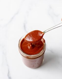 Overhead shot of a small glass mason jar filled with red enchilada sauce with a spoon of the sauce.