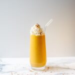 Pumpkin protein shake in a clear glass, topped with whipped cream, with a glass straw.