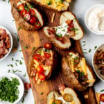 Overhead shot of baked potatoes with various toppings including broccoli, cheese, bacon, tomatoes, and chives.
