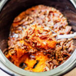 Big scoop of sweet potato casserole topped with pecans in a slow cooker.
