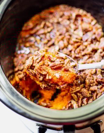 Big scoop of sweet potato casserole topped with pecans in a slow cooker.