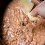 A chip being dipped into a crockpot bean dip.