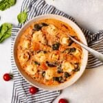Overhead shot of a white bowl filled with crockpot tortellini soup on top of a striped blue napkin and white background.