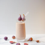 Side shot of a fig smoothie topped with figs in a clear glass with a glass straw.