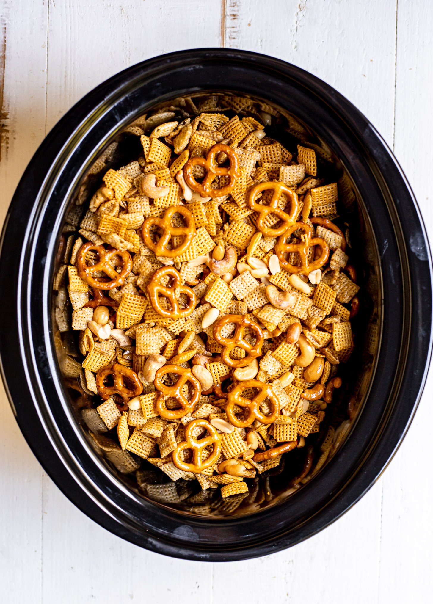 Overhead shot of Chex Mix in a slow cooker, including rice Chex, corn Chex, pretzels, peanuts, and cashews.