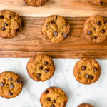 Nine chocolate chip muffins arranged on a wooden and marble surface, viewed from above.